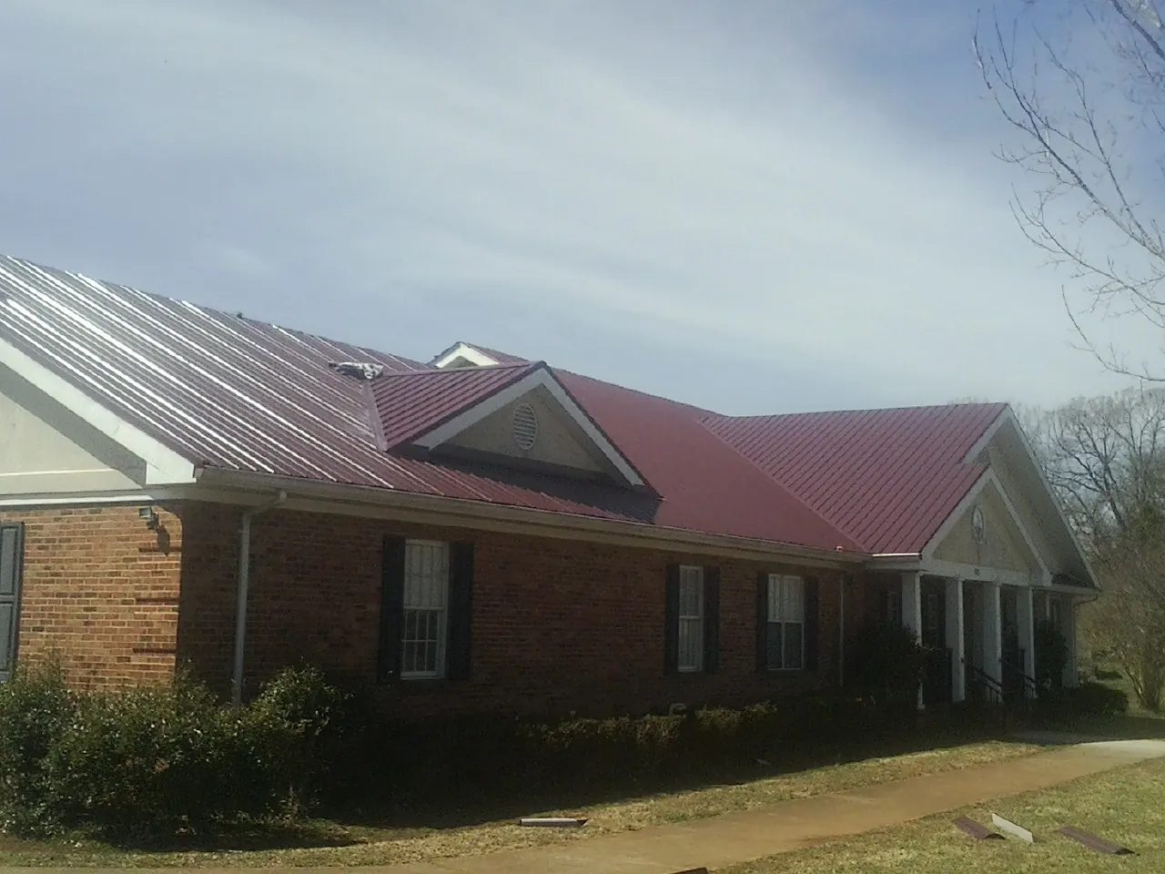 Red metal roof with gabled entries on a long brick building, from a Hail Damage Roof Repair job in Transfer