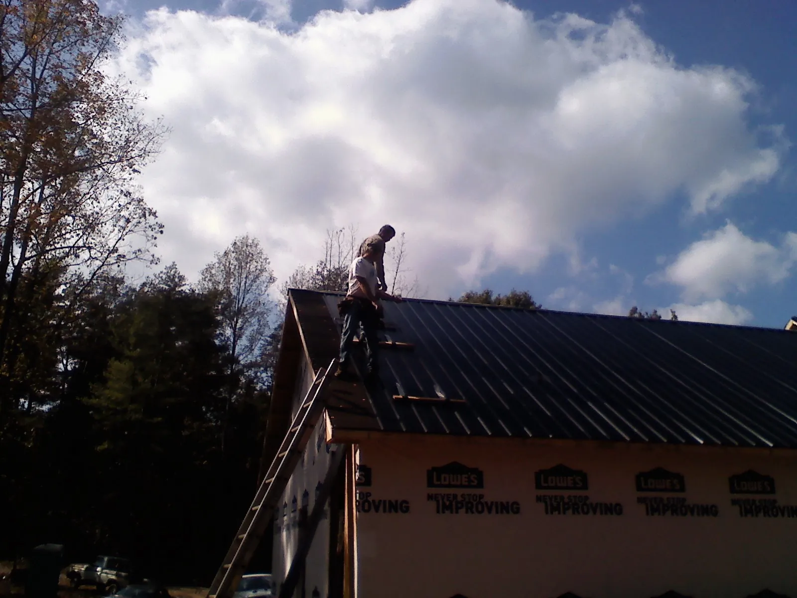 Roofer fastening dark metal panels high against a cloudy sky, from a Roof Inspection job in Transfer