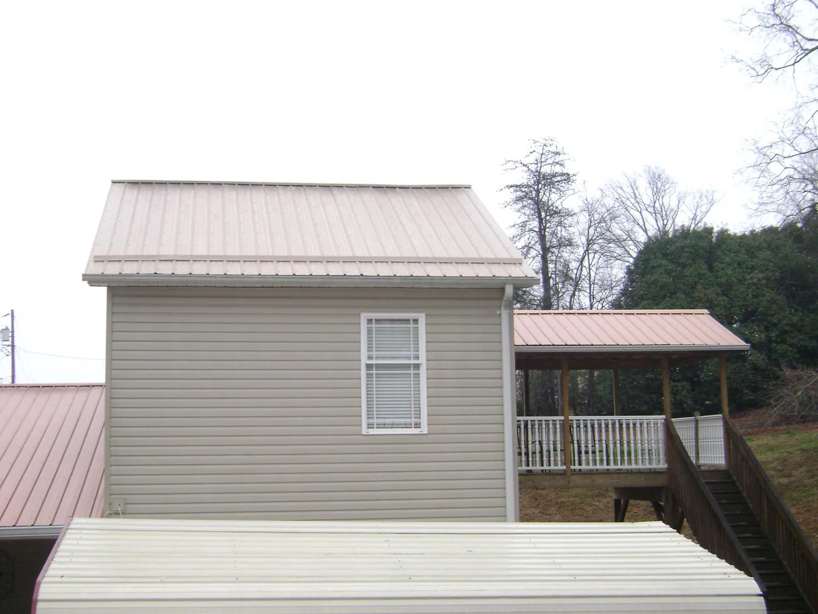 Tan metal roofs on a two story addition and attached porch, from a Roof Replacement job in Transfer