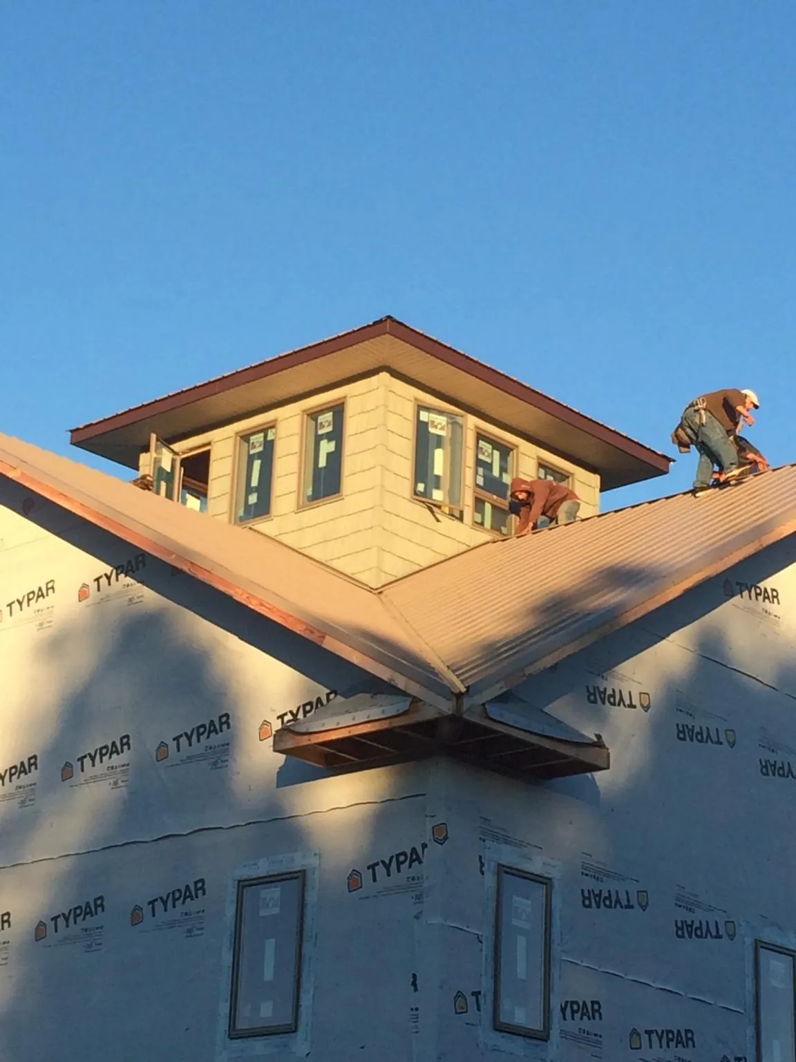 Roofers working around a rooftop cupola on a new metal roof at sunset — Roof Waterproofing in Transfer by Roofing Brothers